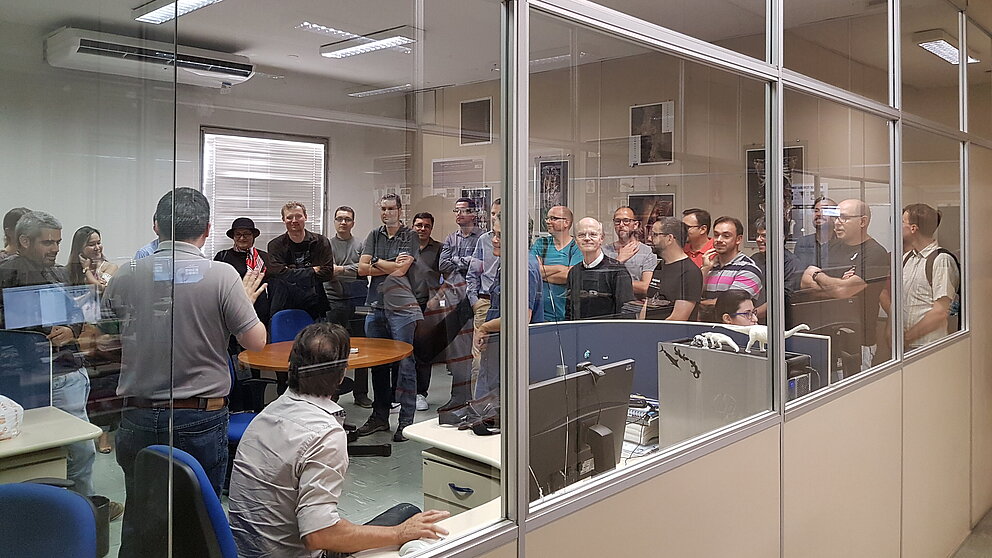 Eine Gruppe von Leuten steht in einem Büro und hört den Erklärungen eines Mannes zu. (Brazilian-German Frontiers of Science and Technology Symposium 2016)