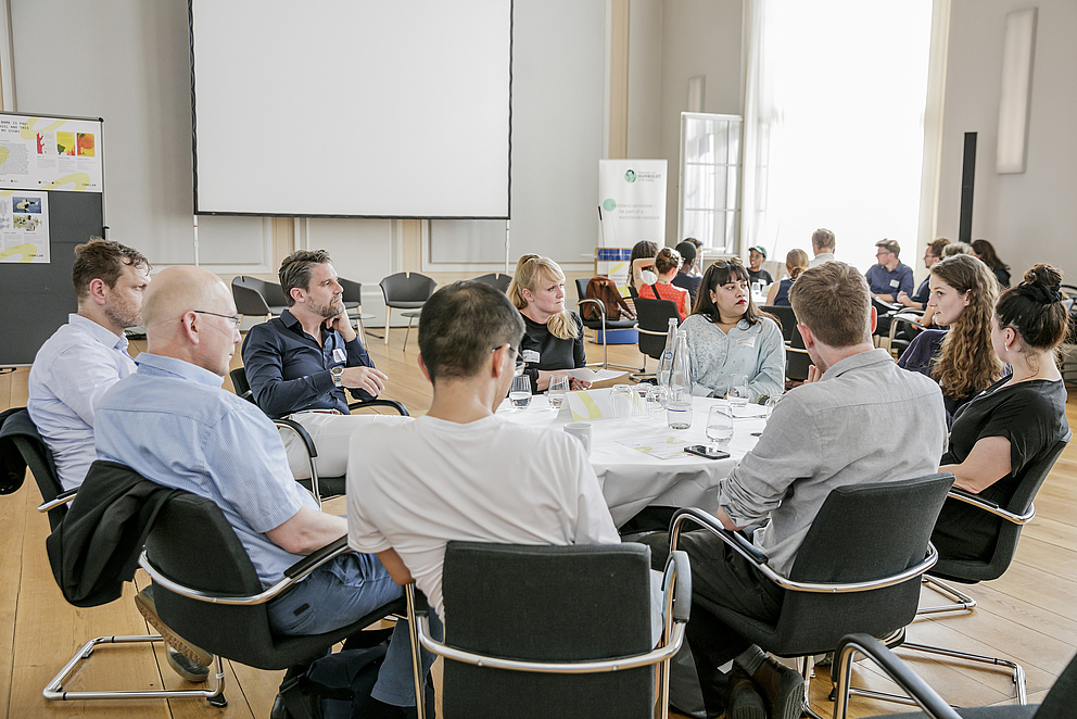 Die Teilnehmenden des Events sitzen um einen runden Tisch und diskutieren. 