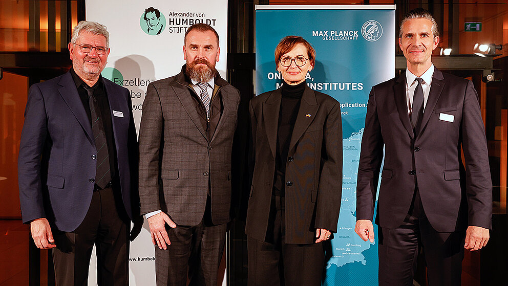 Vier Personen - drei Männer und eine Frau - stehen auf einer Bühne vor den Bannern der Humboldt-Stiftung und der Max-Planck-Gesellschaft.
