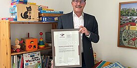 Der stellvertretende Generalsekretär Thomas Hesse präsentiert das Zertifikat audit berufundfamilie im Eltern-Kind-Raum