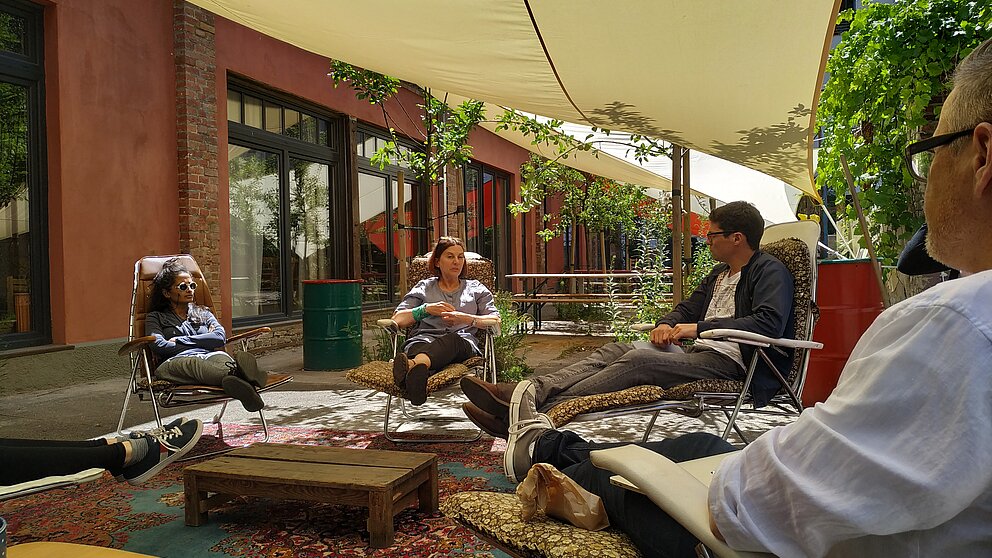Vier Menschen auf Liegestühlen um einen Gartentisch diskutieren miteinander.