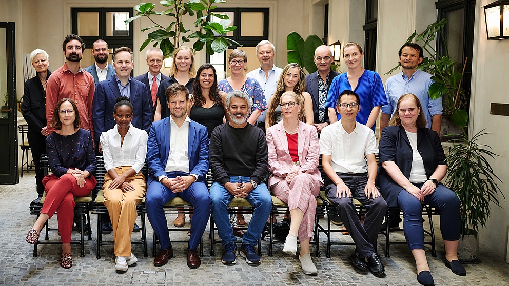 Gruppenfoto mit 20 Personen: 7 Personen sitzen auf Stühlen nebeneinander, 13 Personen stehen dahinter.