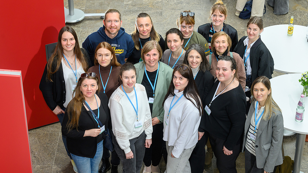 Eine Gruppe von 16 Leuten ist aus der Vogelperspektive zu sehen. Sie lächeln in die Kamera. 