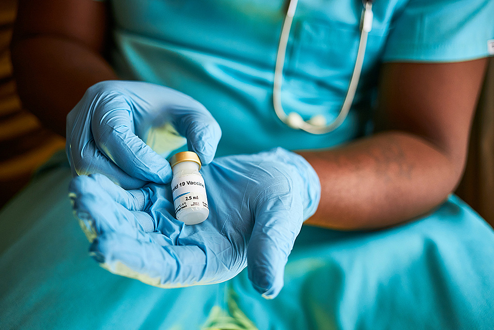 Stockfoto: Eine Person in Laborkleidung hält ein Fläschchen, auf dem COVID-19 Vaccine steht. 