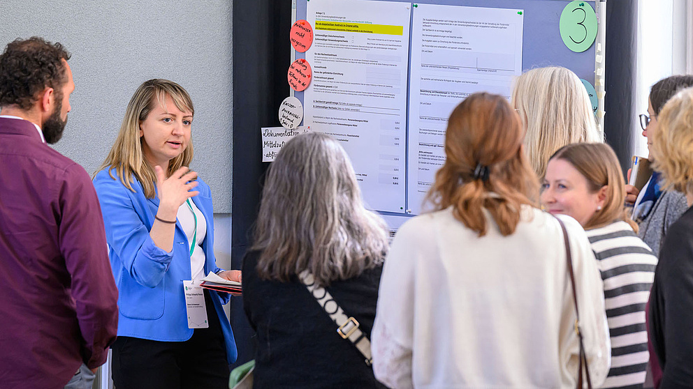 Menschen stehen vor einem Poster, eine Frau erklärt etwas.