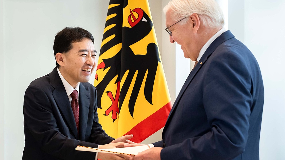 Zwei Männer, lachend bei der Urkundenübergabe 