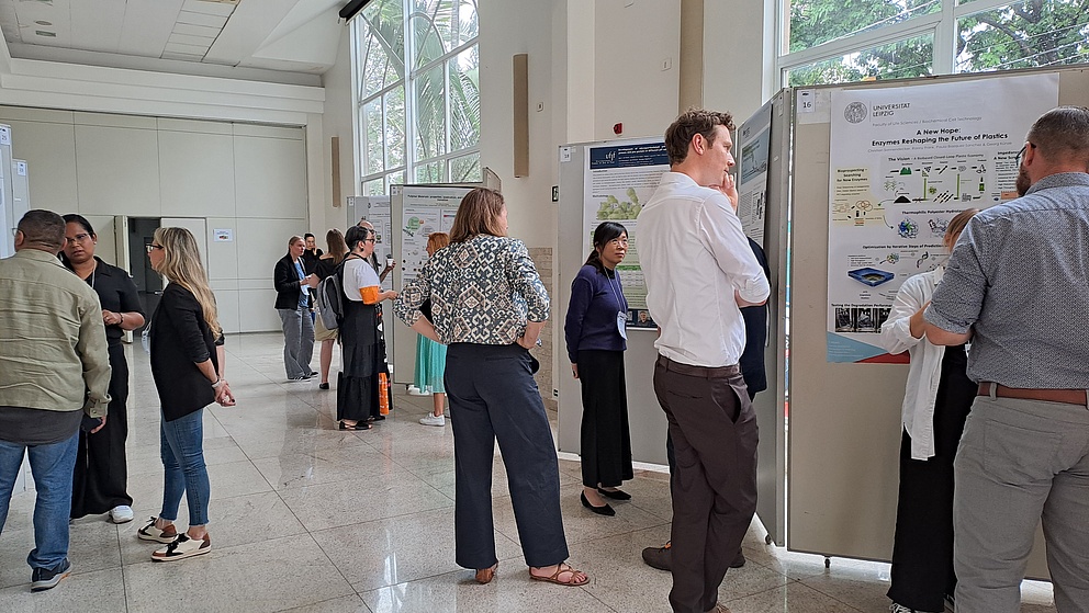 Teilnehmer einer Konferenz stehen um Poster, die wissenschaftliche Informationen über Enzyme und Plastik präsentieren.