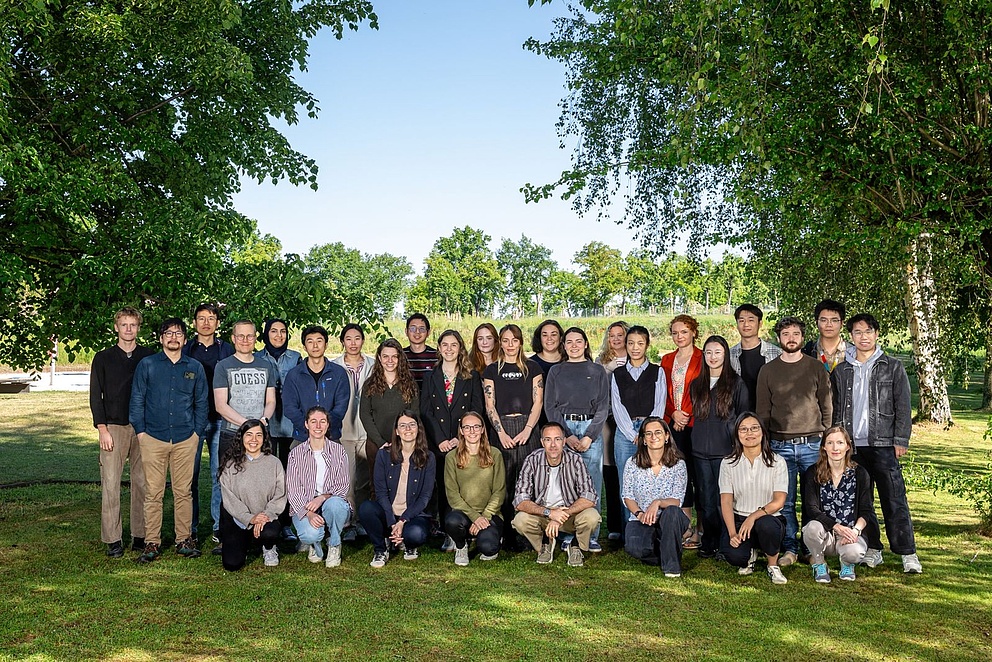 Das Foto zeigt Silvia Vignolini mit ihrer rund 30-köpfigen Forschungsgruppe am Max-Planck-Institut in Potsdam. Die Gruppe steht auf einem Rasen, im Hintergrund sind Bäume und ein Feld zu sehen.