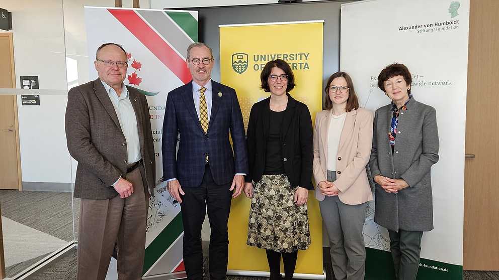 Fünf Menschen, drei Frauen und zwei Männer, stehen in einem Raum aufgereiht und lächeln in die Kamera. 