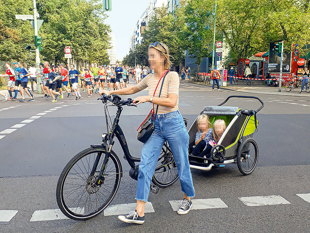 Eine Frau schiebt ein Fahrrad mit Kinderanhänger über die Straße