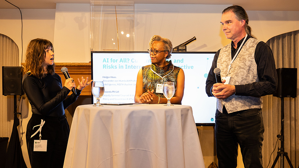 Zwei Frauen und ein Mann auf einem Podium sprechen miteinander.