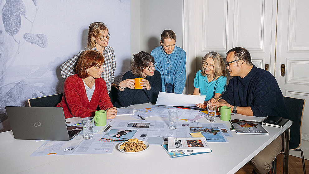 In einem hellen Raum arbeiten mehrere Menschen zusammen, um Ideen auszutauschen, während sie auf Dokumente und Bilder blicken.