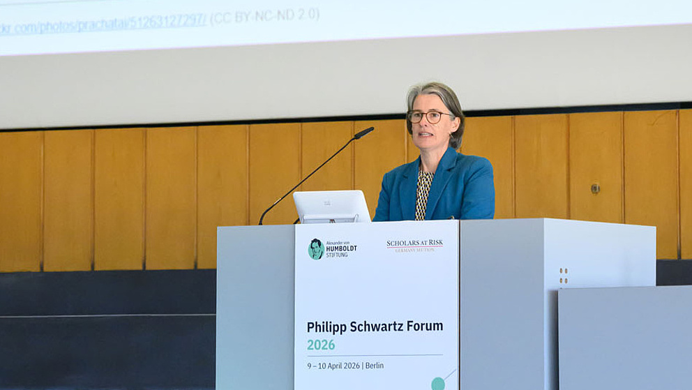 Person steht hinter einem Podium auf einer Bühne. Hinter ihr sieht man eine Päsentation, auf der steht "What is the state of academic freedom around the world?"