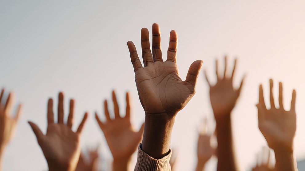 Hände in verschiedenen Hauttönen heben sich, um eine Botschaft der Einheit und des gemeinsamen Ziels zu vermitteln.