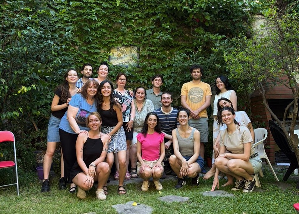 Das Gruppenfoto zeigt Paula Tribelli, ihre Forschungsgruppe und vier weitere Kolleg*innen im Garten der Universität Buenos Aires. Alle lächeln glücklich. Tribelli ist in der Mitte und trägt ein pinkes T-Shirt.