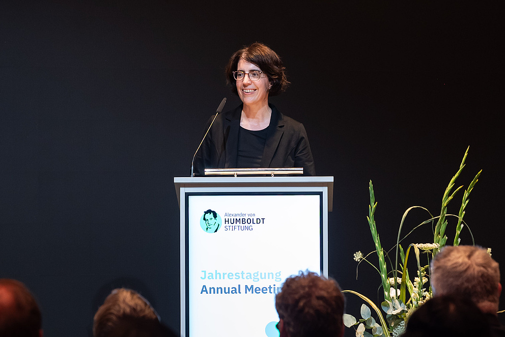 Eine Frau steht auf einer Bühne hinter einem Podium.