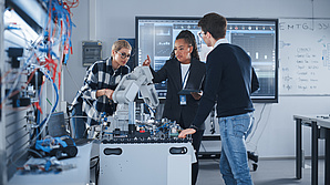 Die Gruppe von Fachleuten analysiert einen Roboterarm, umgeben von technischen Geräten und Bildschirmen, die Daten anzeigen.