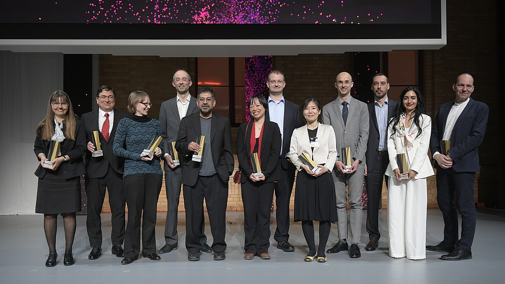 Gruppenfoto mit Menschen auf einer Bühne, die Preisstelen in den Händen halten