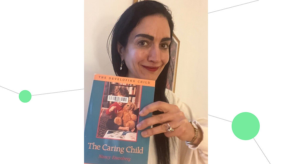 Eine Frau mit langem braunem Haar (Tina Malti) hält lächelnd ein Buch in die Kamera, geschrieben von der Entwicklungspsychologin Nancy Eisenberg. Drumherum ist eine Netzwerkgrafik mit hellgrünen Verbindungspunkten zu sehen
