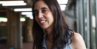 Das Portrait-Foto zeigt Paula Tribelli in der Universität Buenos Aires. Sie hat dunkles, mittellanges Haar und trägt ein hellblaues Oberteil.