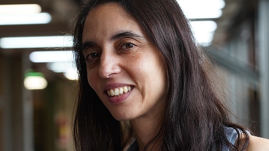Das Portrait-Foto zeigt Paula Tribelli in der Universität Buenos Aires. Sie hat dunkles, mittellanges Haar und trägt ein hellblaues Oberteil.