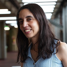 Das Portrait-Foto zeigt Paula Tribelli in der Universität Buenos Aires. Sie hat dunkles, mittellanges Haar und trägt ein hellblaues Oberteil.