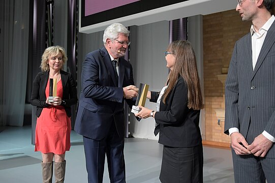 Stiftungspräsident Robert Schlögl schüttelt die Hand von Hanna Kooko, mit Staatssekretärin Döring im Hintergrund