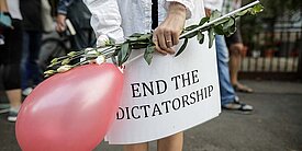 Eine Person hält einen pinken Ballon und ein Schild auf dem steht "end the dictatorship"
