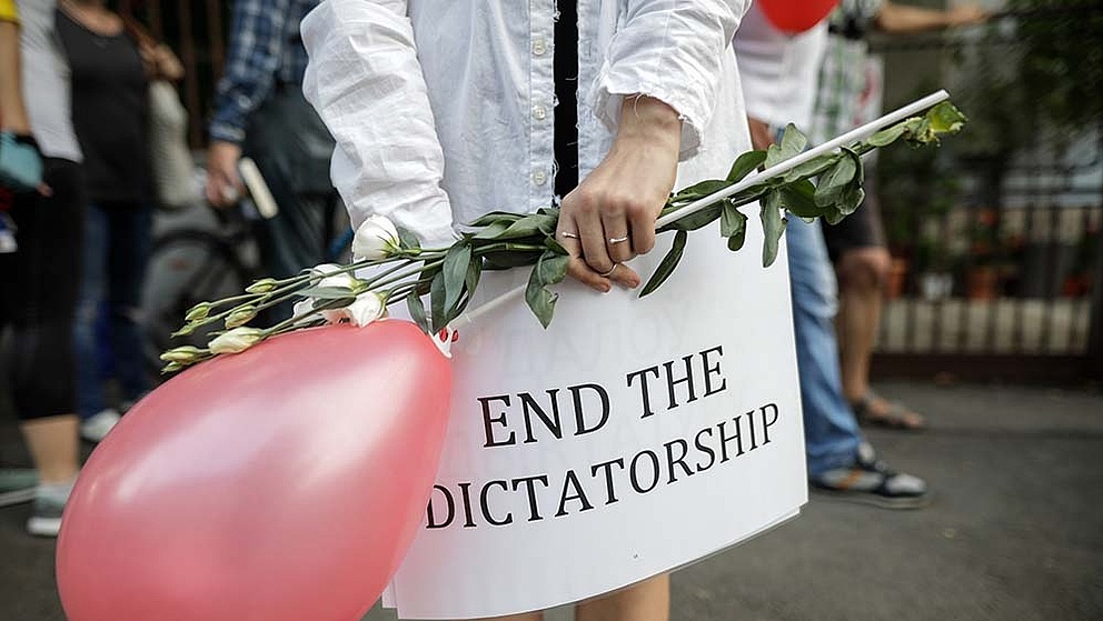 Eine Person hält einen pinken Ballon und ein Schild auf dem steht "end the dictatorship"