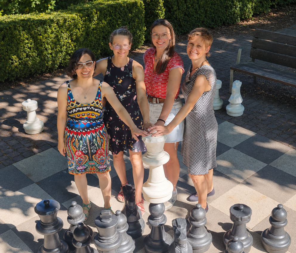 Das Foto zeigt Bettina Frohnapfel mit ihren Koautorinnen Ute Schmitgen, Carola Schmidt und Patricia Sújar-Garrido. Sie stehen lächelnd auf einem großen Schachbrett im Park und haben ihre linken Hände auf eine weiße Königin gelegt.