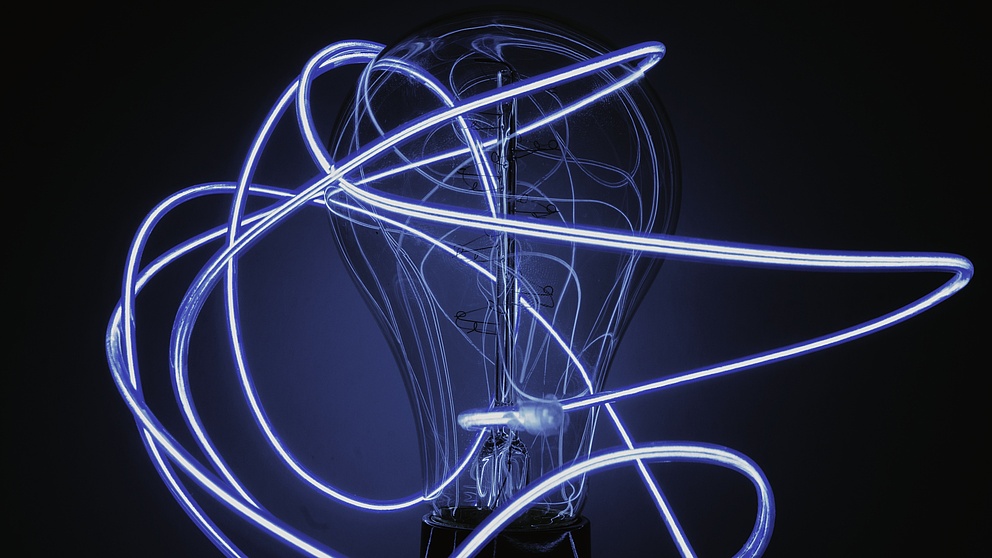 Glühbirne umgeben von dünnen Lichtschläuchen, in dunkelblau gehalten. 