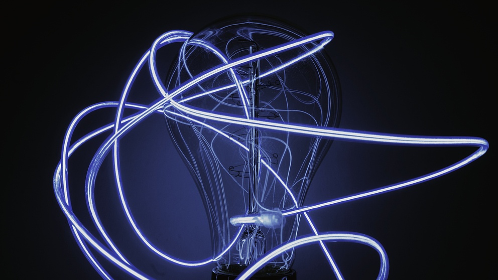 Glühbirne umgeben von dünnen Lichtschläuchen, in dunkelblau gehalten. 