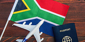 Symbolbild mit Südafrika-Flagge, Modellflugzeug und Reisepass