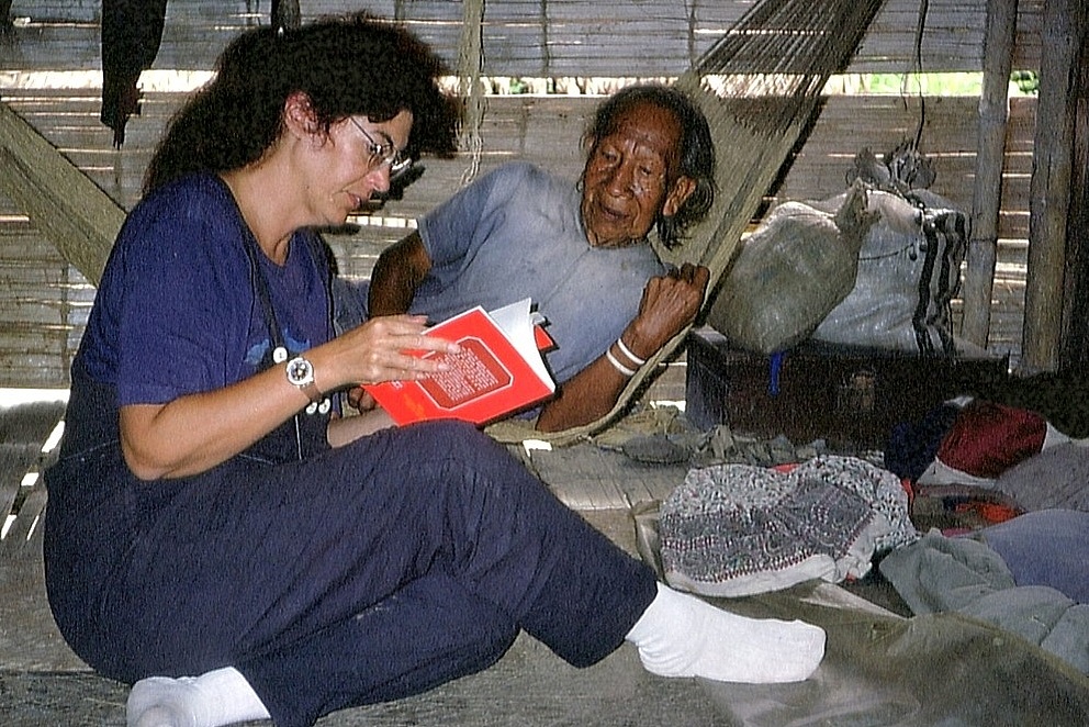 Eine Frau sitzt mit einem Buch auf dem Boden und unterhält sich mit einem Mann, der in einer Hängematte liegt