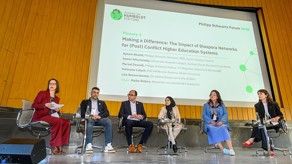 Sechs Menschen auf Stühlen auf einer Bühne 