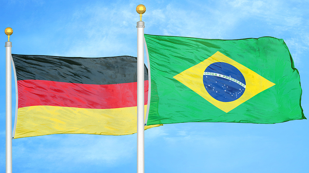 eine deutsche und eine brasilianische Flagge wehen vor einem blauen Himmel