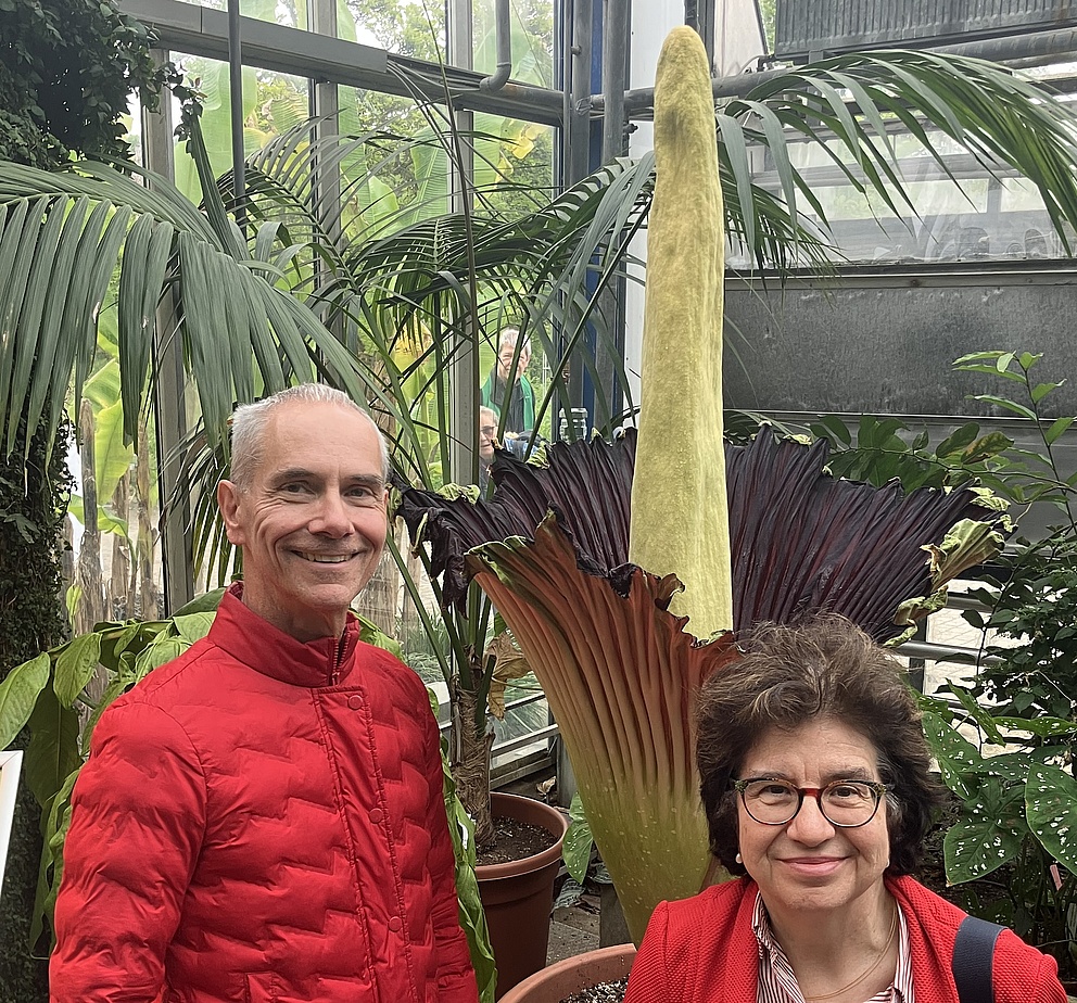 Martina Havenith and AvH Research Award winner Martin Gruebele during a visit to the Botanical Garden of Ruhr University Bochum. Martina Havenith is wearing a red jacket, while Martin Gruebele is also dressed in a red jacket. A large plant can be seen in the background.