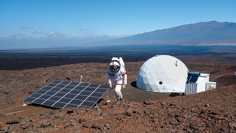 Astronaut*in in einer Vulkanlandschaft mit Zelt und Sonnenkollektoren