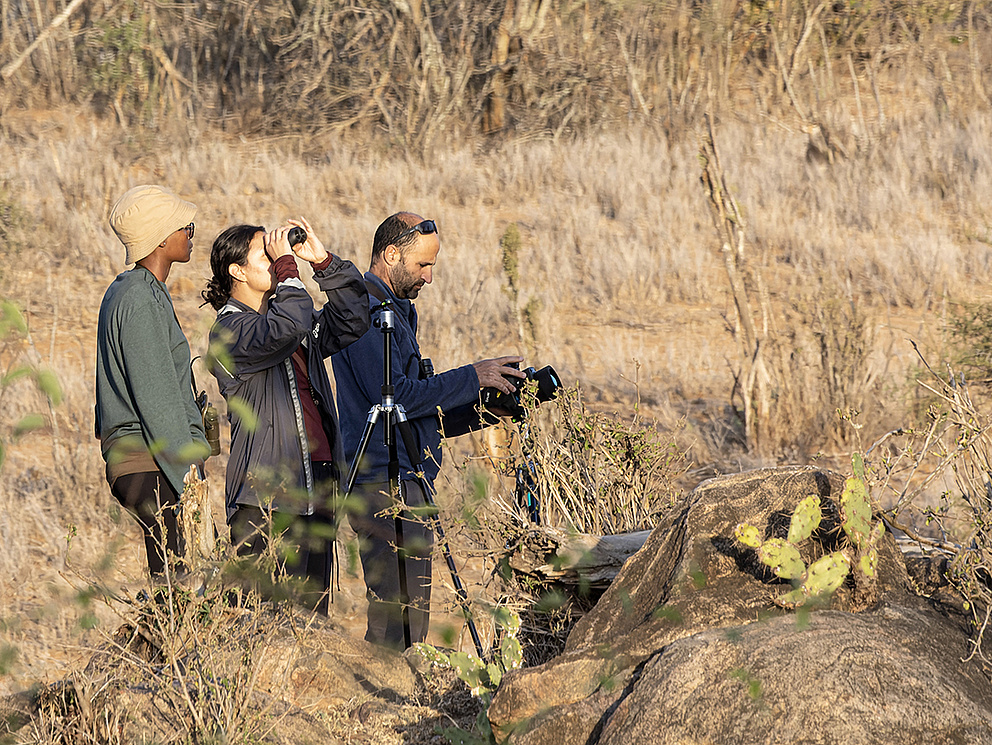 Drei junge Menschen mit Kamera und Feldstecher in einer Steppenlandschaft mit Kaktus