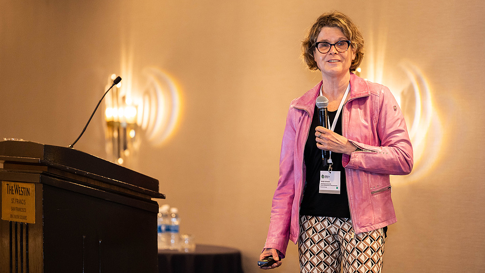 Eine Frau steht auf einer Bühne hinter einem Rednerpult und spricht zum Publikum