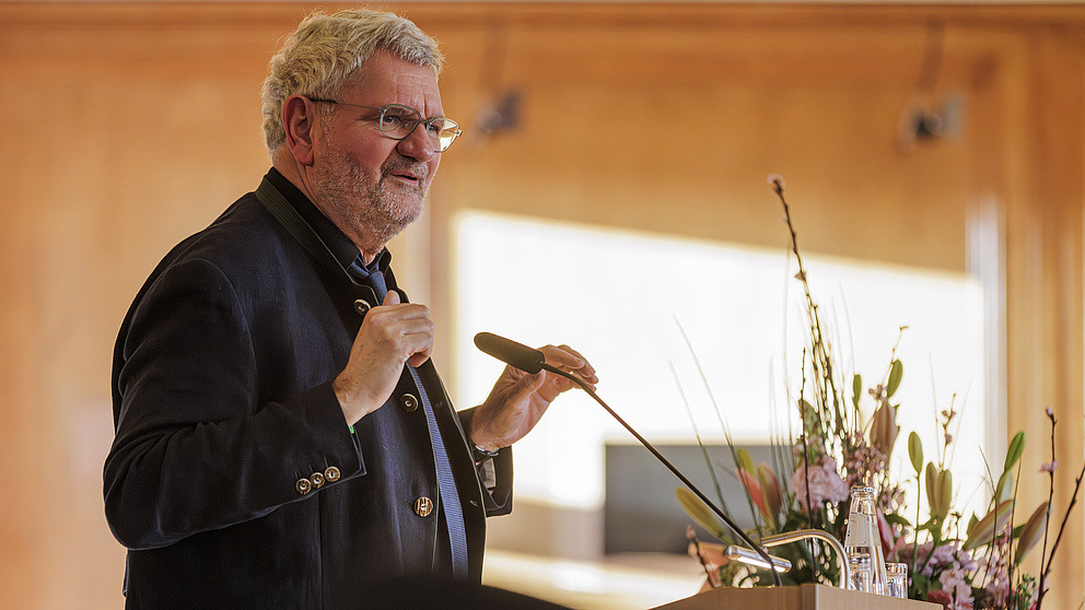 Ein Mann steht auf einer Bühne und spricht in ein Mikrofon.