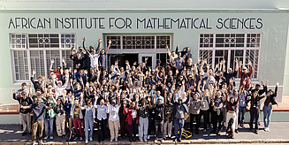 Eine große Gruppe von Menschen steht vor dem African Institute for Mathematical Sciences und hebt die Hände in die Luft.