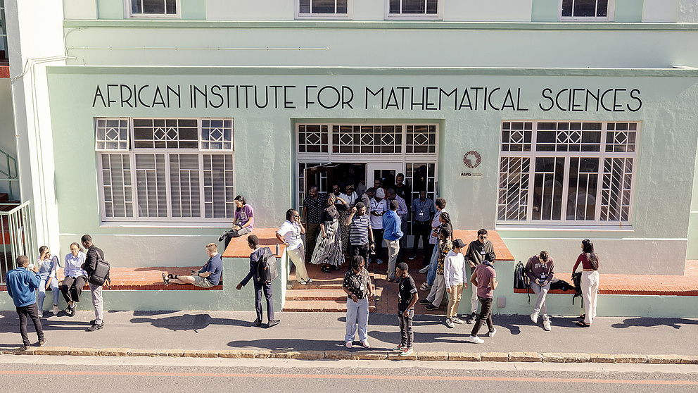 Eine Gruppe von Menschen versammelt sich vor dem African Institute for Mathematical Sciences, während einige auf der Mauer sitzen.
