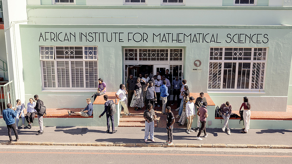 Eine Gruppe von Menschen versammelt sich vor dem African Institute for Mathematical Sciences, während einige auf der Mauer sitzen.