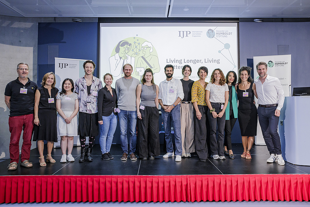 Eine Gruppe von Menschen steht auf einer Bühne. Alle lachen in die Kamera. 