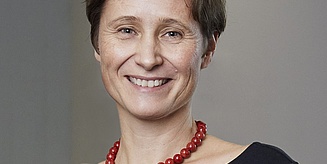 Das Porträtfoto zeigt Bettina Frohnapfel, die in die Kamera lächelt. Sie hat kurzes braunes Haar, trägt ein schwarzes Oberteil und eine rote Perlenkette.