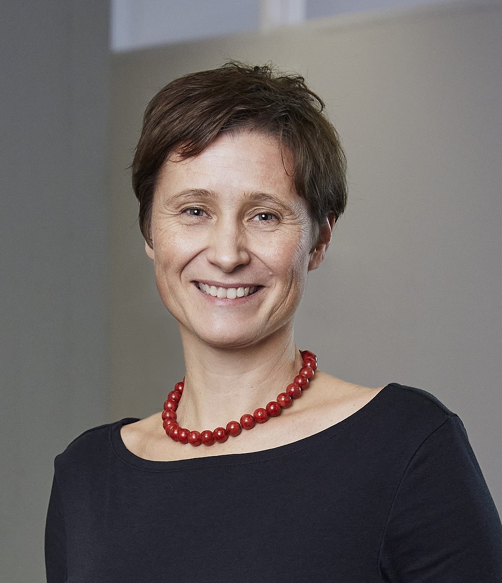 Das Porträtfoto zeigt Bettina Frohnapfel, die in die Kamera lächelt. Sie hat kurzes braunes Haar, trägt ein schwarzes Oberteil und eine rote Perlenkette.