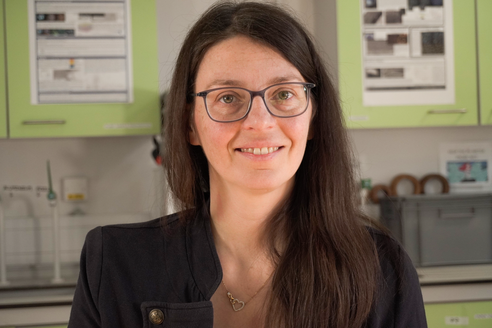 Silvia Vignolini lächelt in die Kamera. Sie hat lange braune Haare und grüne Augen und trägt eine schwarze Jacke. Im Hintergrund ist ein Labor zu sehen.