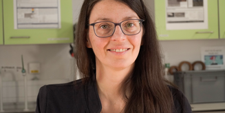 Silvia Vignolini lächelt in die Kamera. Sie hat lange braune Haare und grüne Augen und trägt eine schwarze Jacke. Im Hintergrund ist ein Labor zu sehen.