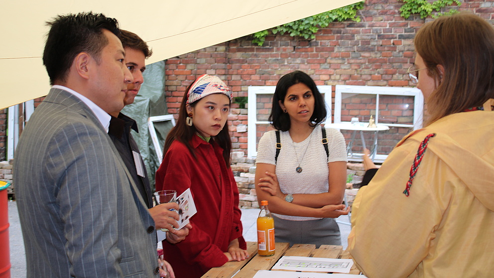 Fünf Personen stehen um einen Tisch in einem Garten und diskutieren